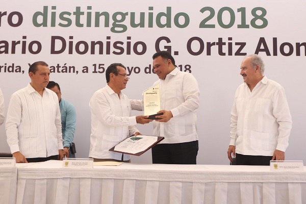 El C. Gobernador del Estado entregando el reconocimiento de “Maestro Distinguido 2018” a Enrique Yanuario Ortiz Alonzo. A la derecha, el Secretario de Educación, Prof. Delio Peniche Novelo.